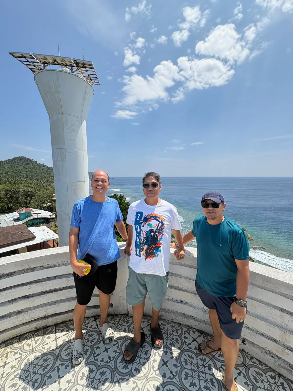 Three hikers on the Cape San Agustin lighthouse viewing deck with the Pacific coastline and the newest tower behind them