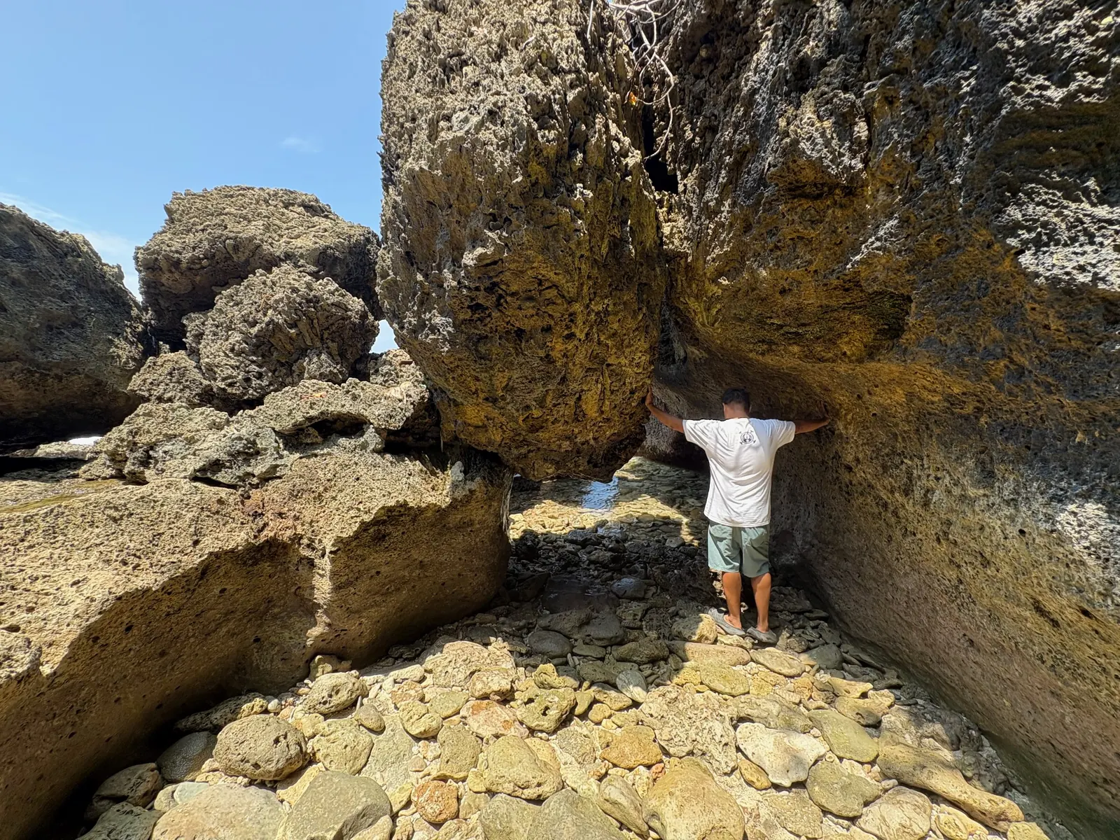 Hiker standing between large coral rock boulders on the low tide shoreline at Cape San Agustin