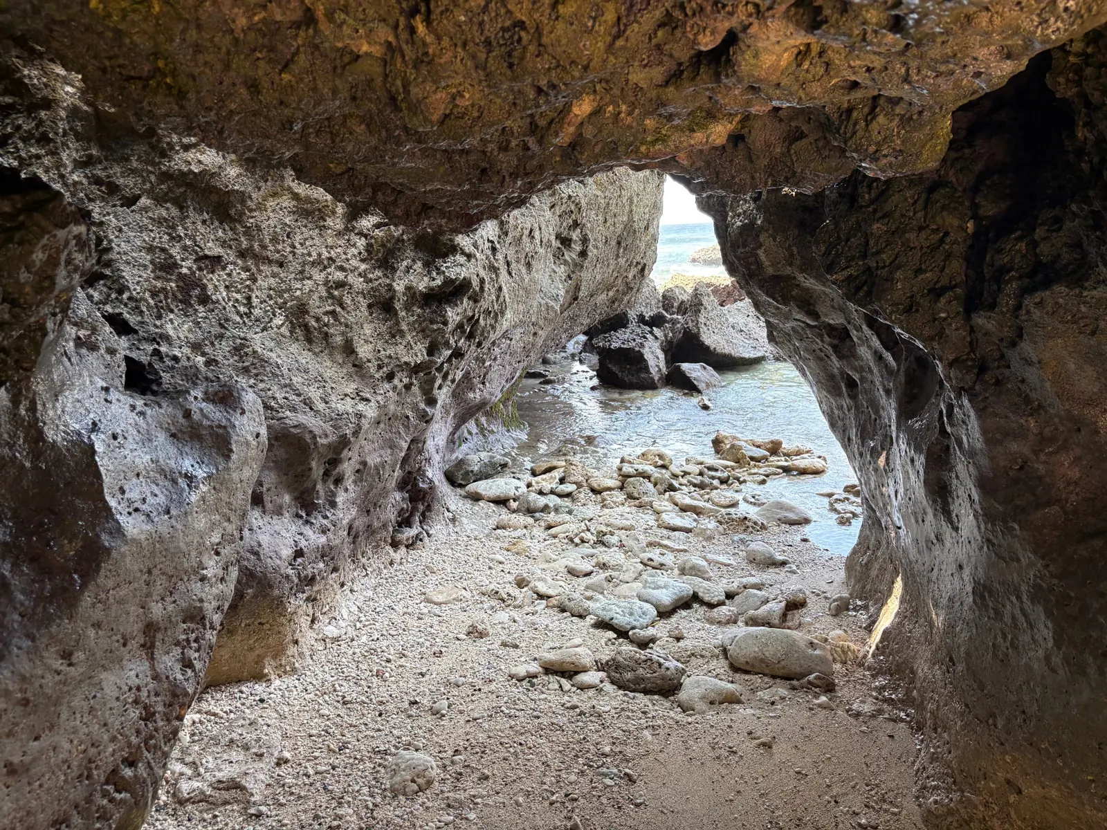 Wave-carved sea cave at Cape San Agustin framing the ocean through a rock opening above a coral-pebble floor