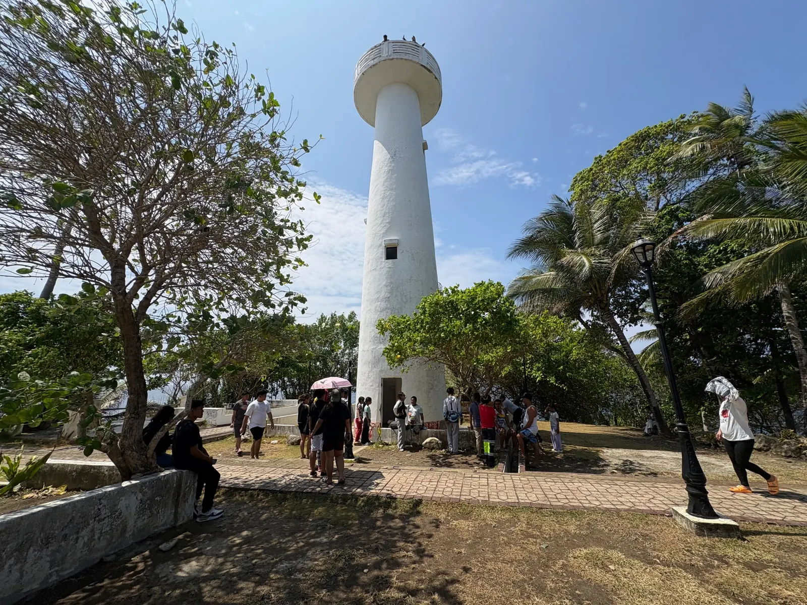 Umbrella-shaped white lighthouse tower at Cape San Agustin Parola surrounded by trees and visitors